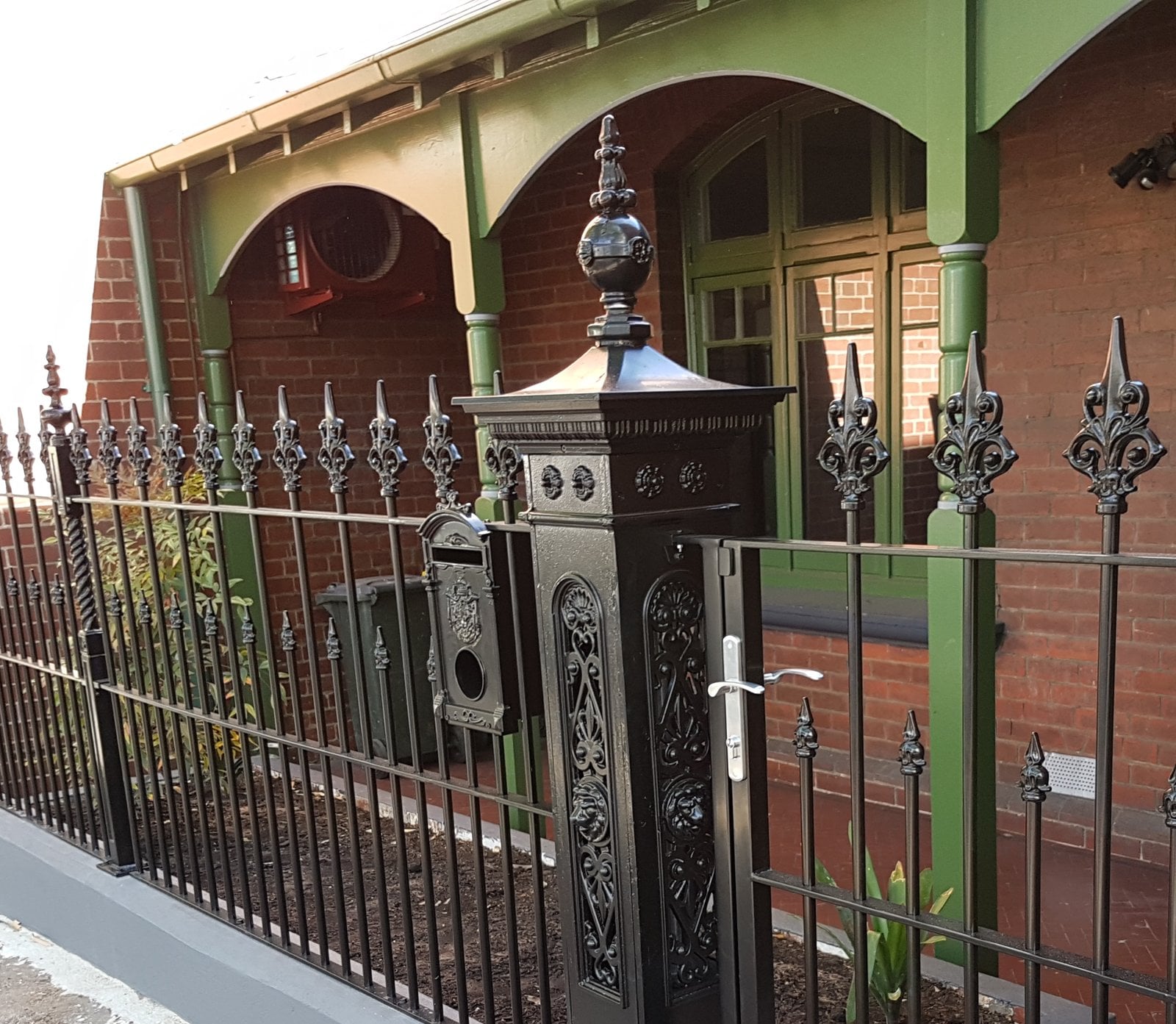 Green timber verandah arches behind restored black cast-iron palisade fencing and pillars, Richmond