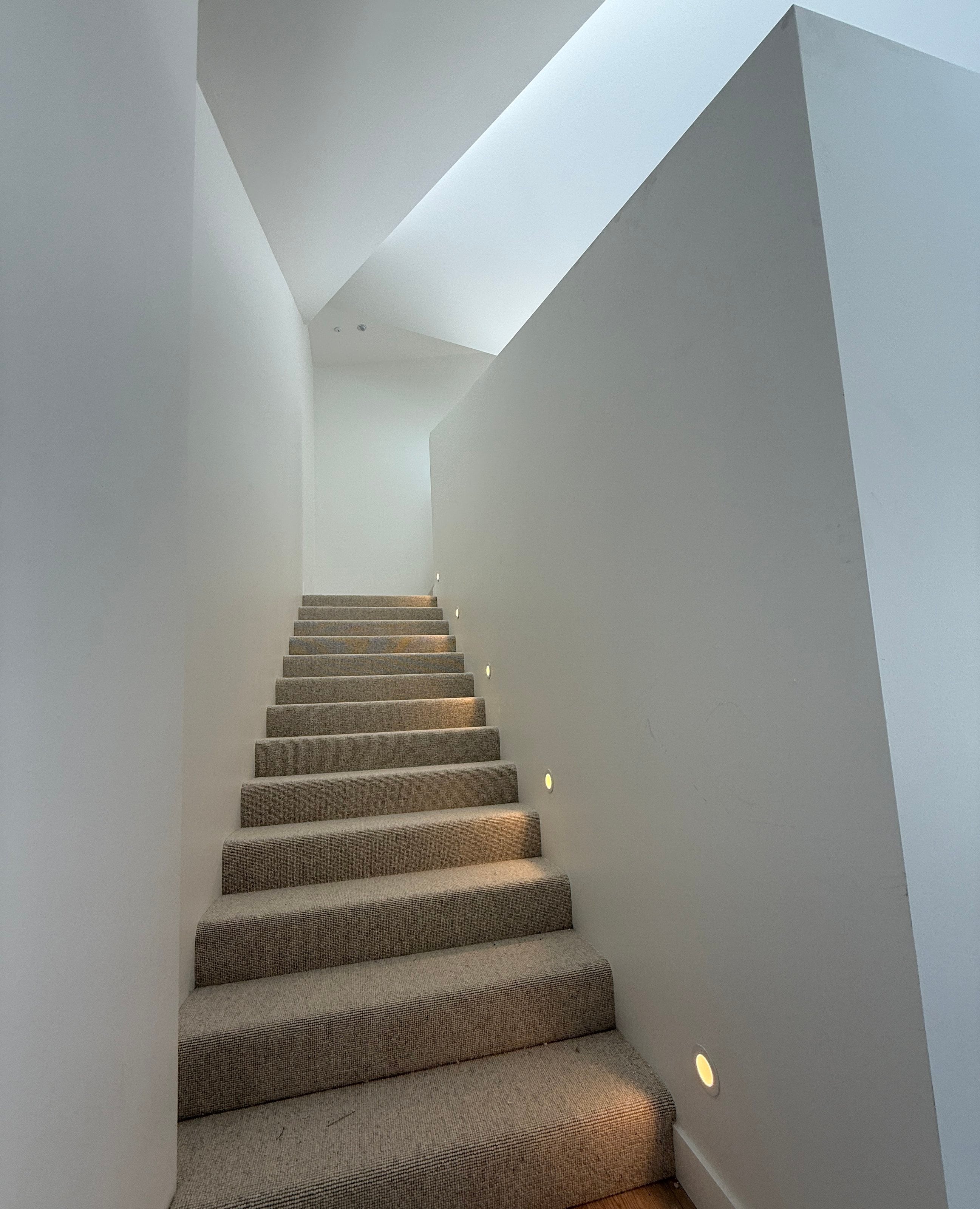 Carpeted stair with step lights rising to a skylight between white walls, Port Melbourne