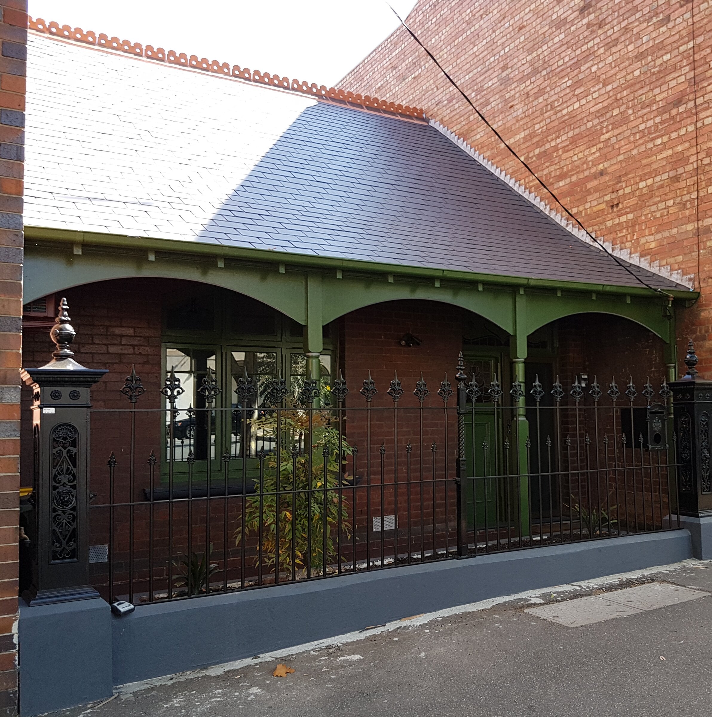 Victorian cottage with a green timber verandah, slate roof and cast-iron fence, Richmond